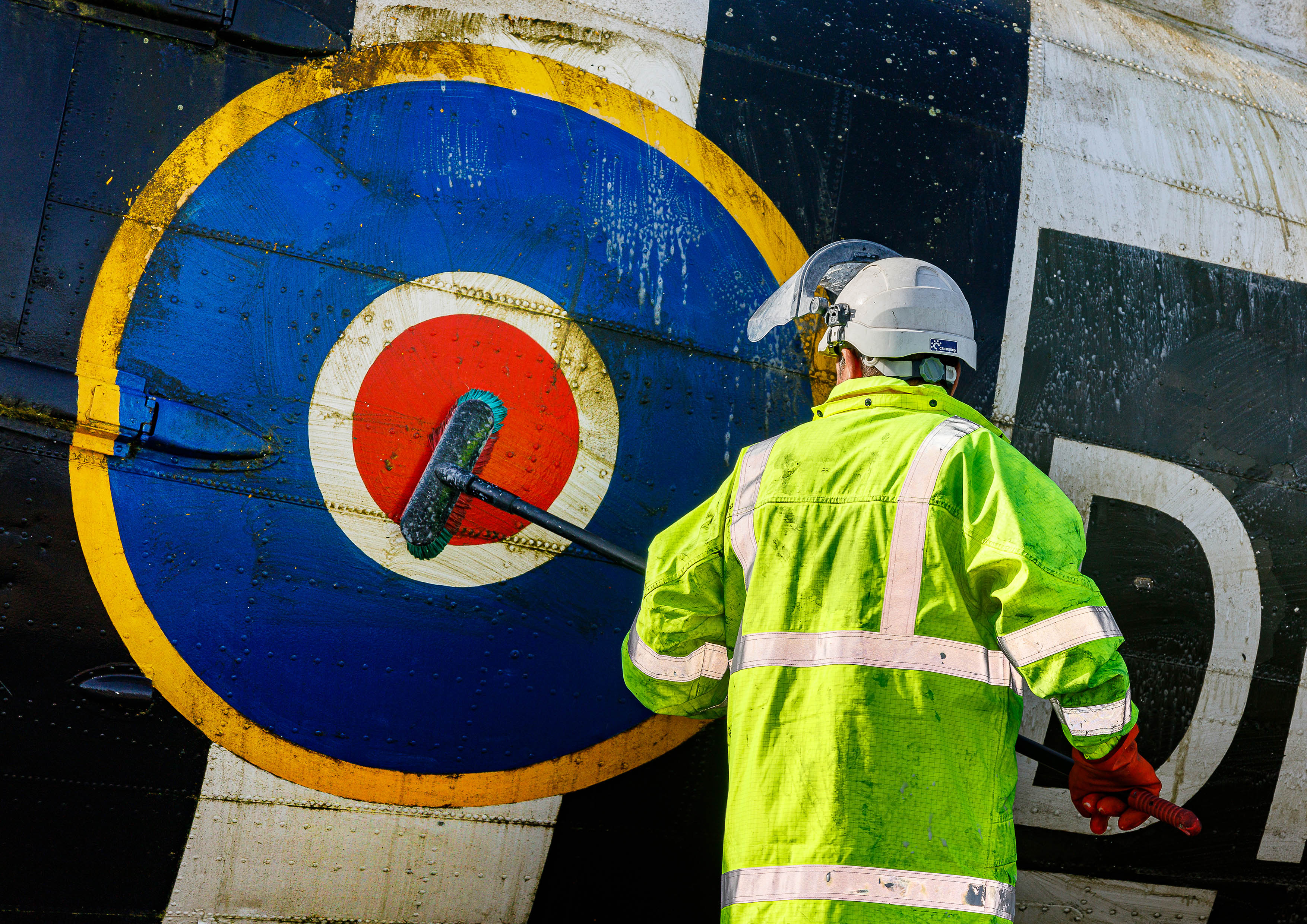 Photo: A member of the Serco Aircraft Wash Team brushing organic debris from the RAF roundel aft of the cargo door